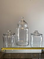 Three clear glass storage jars displayed side by side with a measuring tape showing about 7 inches width for smaller jars.