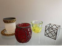 Four decorative glass candle holders displayed on a clear surface against a neutral background, showing details of designs and materials.
