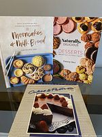 Four cookbooks displayed upright showing titles Moocakes & Milk Bread, Naturally Delicious Desserts, and the third featuring a cake with strawberries on cover.