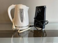 Image showing white electric kettle with attached power cord next to black electric can opener with power cord wrapped around it.