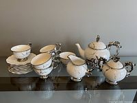 Complete ceramic tea set with teapot, sugar bowl, creamer, cups, and saucers on glass table