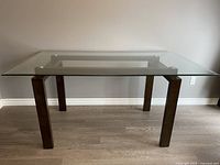 Front view of the rectangular glass dining table with wood legs on a hardwood floor.