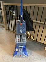 Front view of the upright carpet cleaner placed on carpet showing overall unit with water tanks and handle.