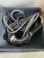 Coiled metal garden hose with attached spray nozzle placed inside a dark container.