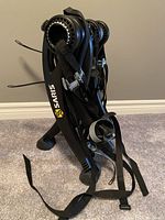 Image of folded Saris black trunk mount bike rack standing upright on carpet with straps and buckles visible