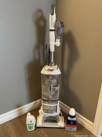Full view of the Shark Navigator Lift-Away vacuum cleaner standing against a wall with two bottles of cleaning liquids on either side (liquids not included in sale).