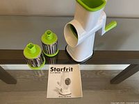 Photo of Starfrit drum grater unit, two grating drums, and instruction manual on dark surface.