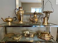 Overview of the set showing teapot, coffee pot, cocktail shaker, tray, chafing dish, butter tray and urn arranged on glass shelving.