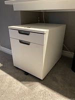 Closed view of white 2-drawer filing cabinet with lock on top drawer, showing smooth finish and built-in handles.