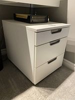 White cabinet with three drawers closed, showing clean design and black recessed handles.