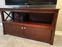 Front view of dark cherry/mahogany wooden TV stand with an open shelf and closed cabinet with metal knobs.