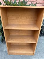 Full view of the wooden bookcase showing three shelves and light brown finish.