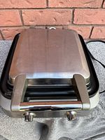 Front view of closed Breville waffle maker showing brushed metal top and handle.