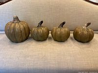 Four ceramic pumpkins in a row on a fabric upholstered surface seen from front