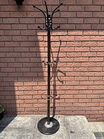 Full view of brown coat rack showing vertical pole, round weighted base, and multiple curved hooks for hanging items