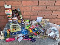 Photo showing stacks of ribbons, craft punches, scissors, adhesive tool, stickers, and stamps arranged on a surface against a brick wall.