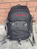 Front view of the black Dakine photography backpack with visible Dakine logo in red and multiple zipper compartments.