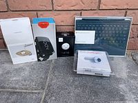 Image shows the full bundle of electronic items arranged on floor: SmartDevil humidifier box, Noon VR box, Philips Hue Tap box, Microsoft Surface Pro 4 type cover in packaging, GriffinSightLight projector in plastic case.