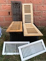Four floor registers arranged, showing variety of materials and slat patterns against brick wall and grass.