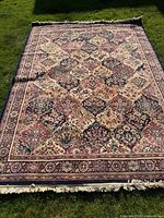 Full view of floral patterned oriental rug laid flat on grass showing entire design and fringe edges.