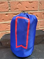 Blue pouch containing the Michelob Ultra running jacket, front side with red outlined rectangular emblem.