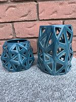 Two blue ceramic candle holders with geometric cut-out designs placed on a textured surface with a brick background.