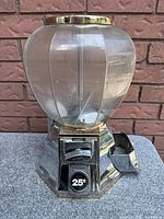 Front view showing the clear dual compartments atop a metal base with 25¢ coin slot and turn handle.