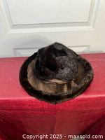 Dark brown fur hat with wide brim and fur trim, ribbed ribbon band, and bow detail resting on a red surface.