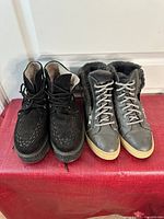 Photo showing two pairs of women's boots on a red surface in front of a white door: black Rose G. creeper boots on the left, grey Cougar winter boots on the right.