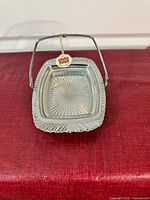 Rectangular serving dish including hinged handle and scalloped edges with glass insert inside.