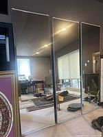 Front view showing three identical full-length rectangular closet door mirrors standing side by side reflecting room interiors.