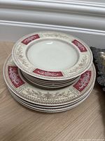 Stack of dinner plates and smaller plates with decorative maroon and beige patterned rims on cream background