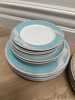 Stack of plates including 6 dinner plates and 6 small plates with aqua blue and silver wave border pattern.