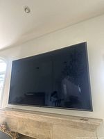 Front view of the 73 inch LG TV mounted on the wall with reflective screen showing part of a room.