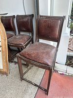 Set of four brown leather bar chairs with wooden frames, showing wear and vintage condition.