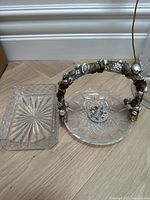 Rectangular glass tray and round crystal dish with decorative handle, shown on wooden floor against white baseboard
