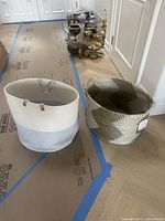 Two hamper baskets on floor, one white and light grey with handles, one black and white zigzag pattern with side handles.