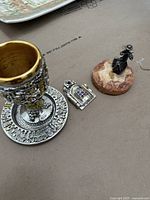 Photo of kiddish cup with gold-tone interior and detailed Jerusalem design base with figurines on cardboard background.