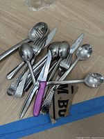 Photo of assorted metal kitchen utensils including spoons, forks, and a knife with textured and plain handles.