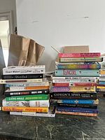 Photo showing a large assortment of books stacked in two piles against a white wall.