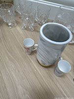 Photo of the glassware grouped together including textured and smooth clear glass pieces with a large marble-effect ceramic vase and small ceramic cups with printed text.