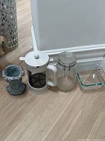 Photo showing four kitchen items and decor: decorative ceramic cup, French press, glass jar, glass dish.