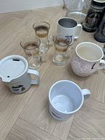 Top view of the set including four clear glass tea glasses and three assorted ceramic mugs on wooden floor.