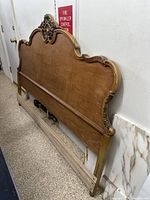 Wooden queen size bed frame with ornate carved headboard, side rails, and footboard supports shown leaning against wall.