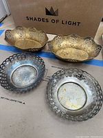 Four silver trays with two large scalloped and two smaller round lattice sides trays arranged on floor.