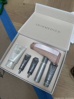 Top view of open Skinmedica branded box containing a cleanser tube, three smaller skincare tubes, a silver spray bottle, and a fabric headband.