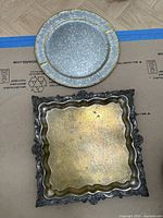 Round speckled gray tray and ornate square silver-plated tray with scalloped edges