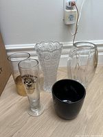 Front and side view of five vases grouped on wooden floor showing varying styles and materials