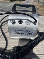 Close-up of Iwata Silver Jet compressor with control knobs, pressure gauge, and coiled hose attached.