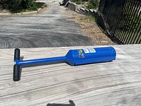 Full view of the blue clam digger with T-handle placed on a wooden surface outdoors.